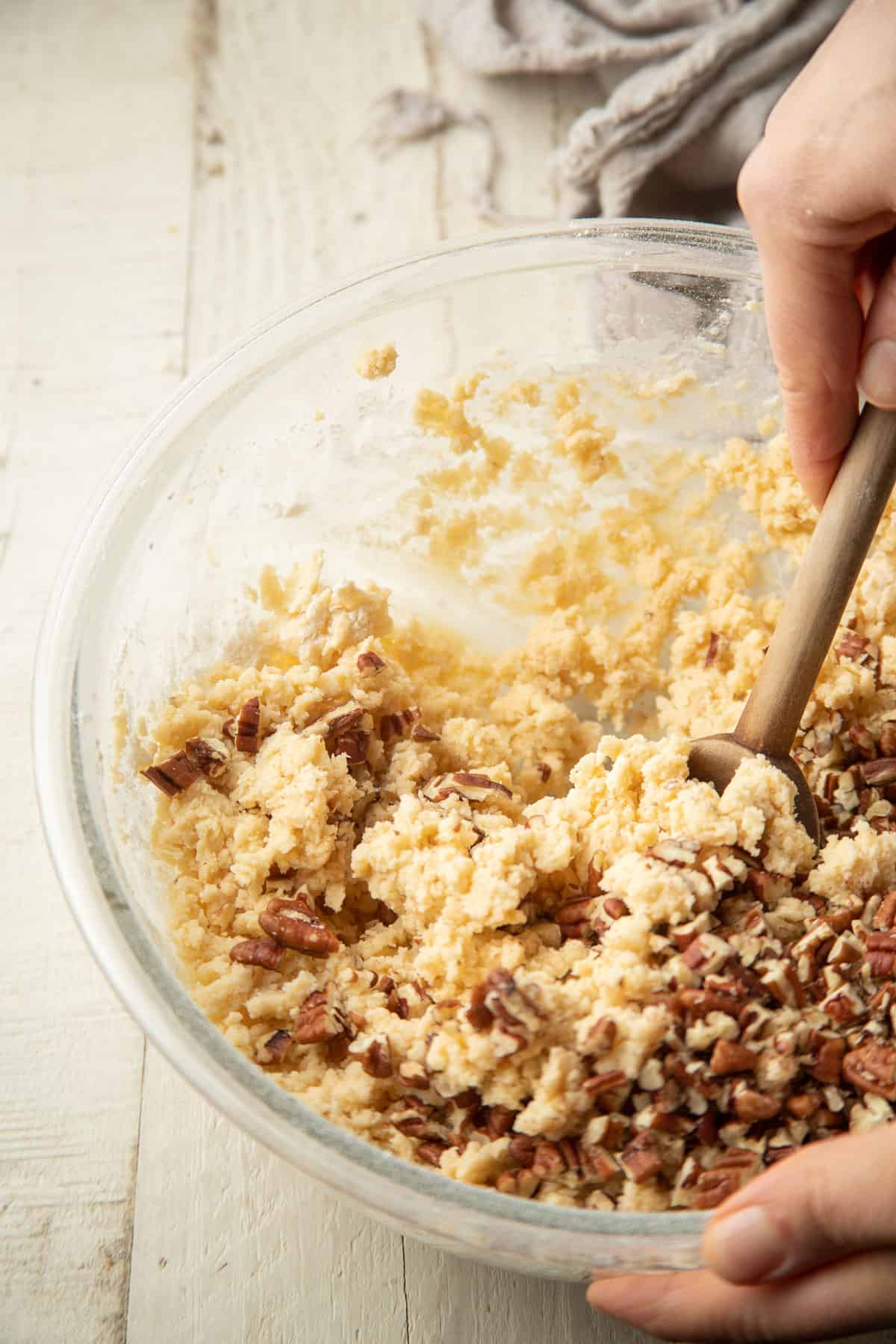 Hand stirring pecans into a bowl of cookie dough.