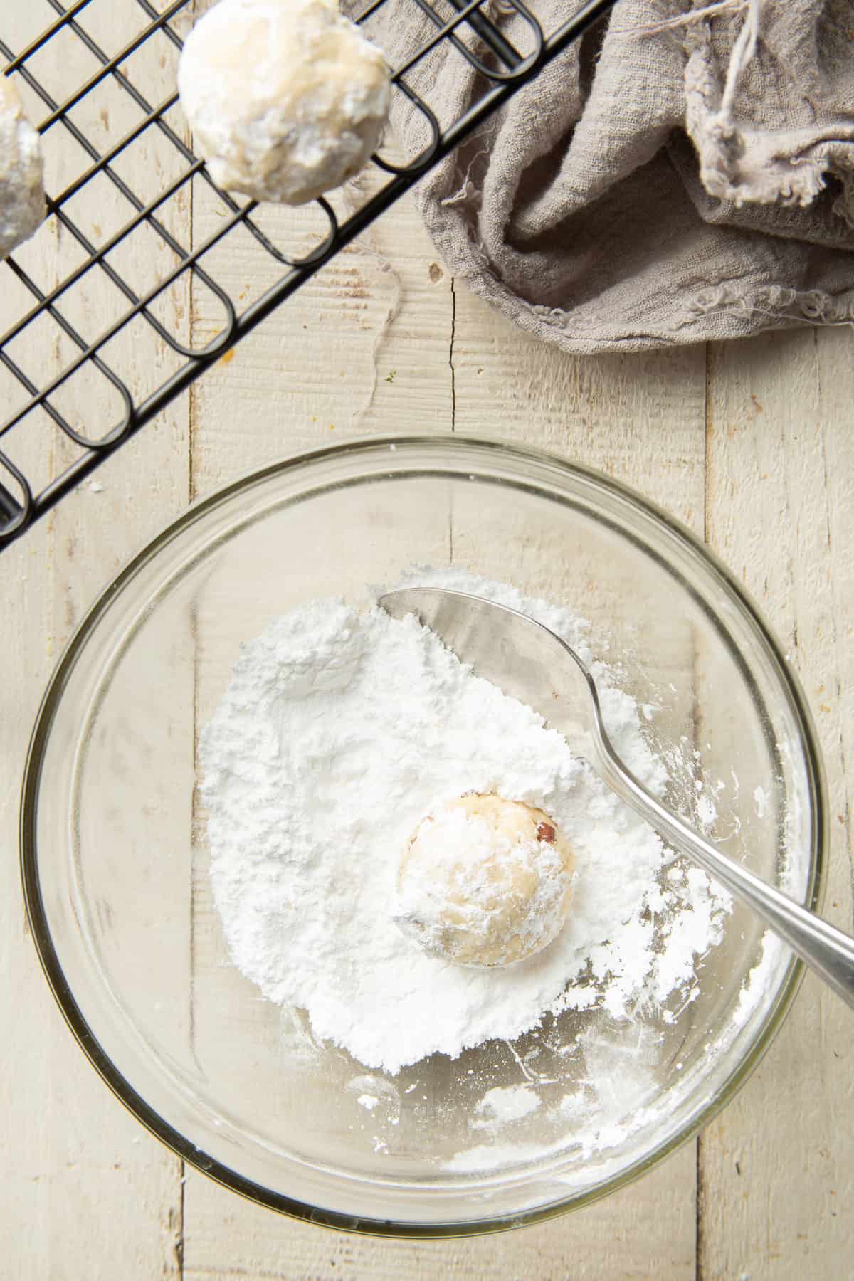 Vegan Snowball Cookie in a bowl of powdered sugar with spoon.