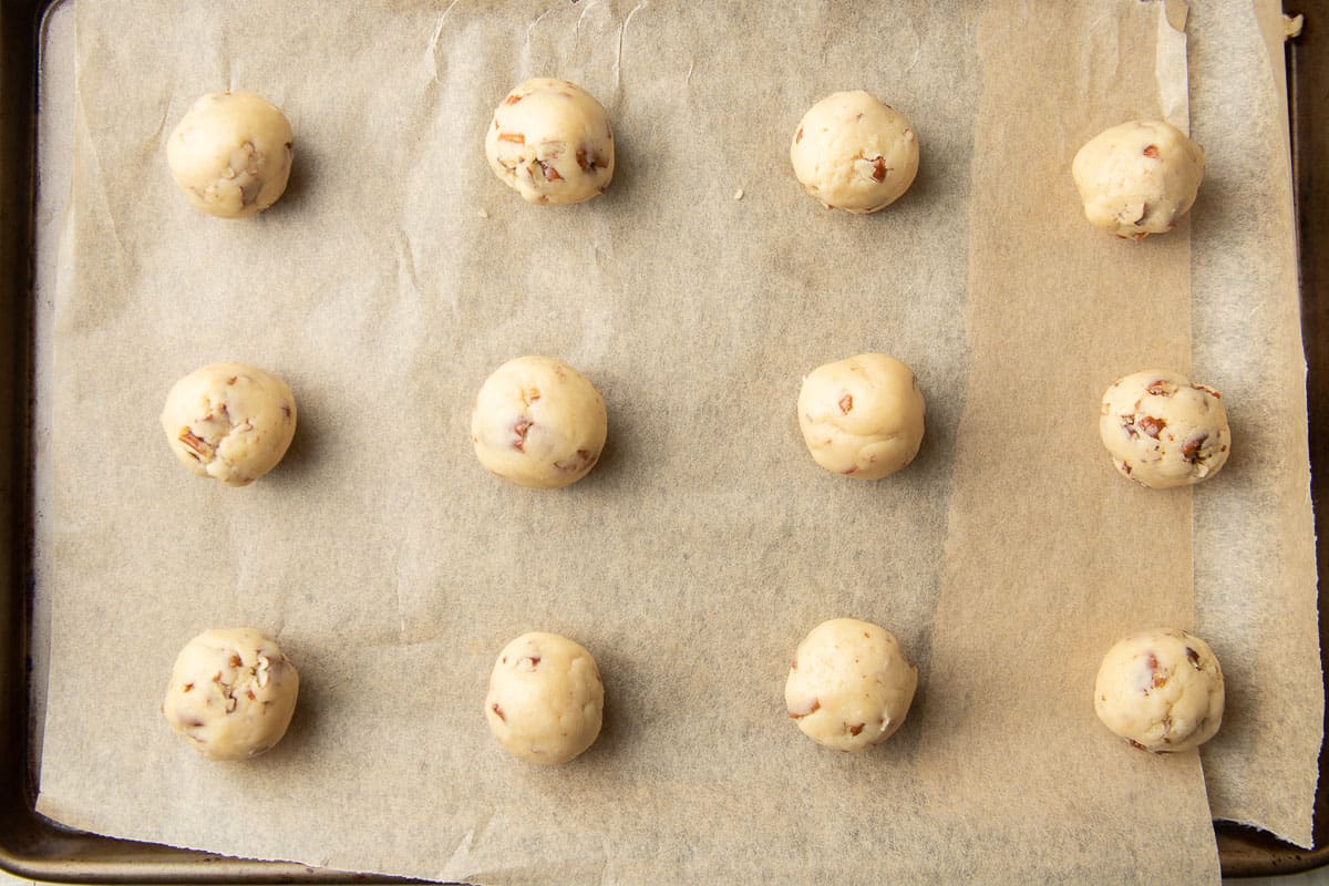 Cookie dough balls on a parchment paper lined baking sheet.
