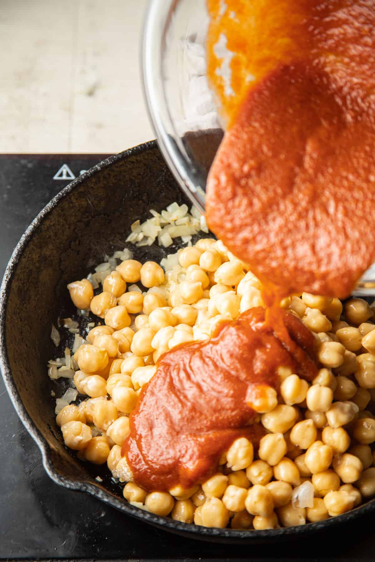 Sauce being poured into a skillet filled with chickpeas.