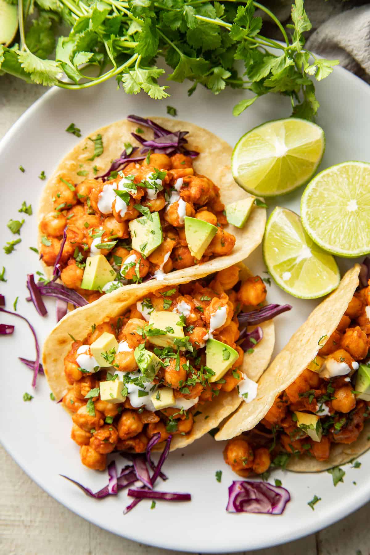 Three Chickpea Tacos and limes on a plate surrounded by fresh cilantro.