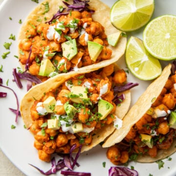 Close up of three Chickpea Tacos on a plate with lime slices.