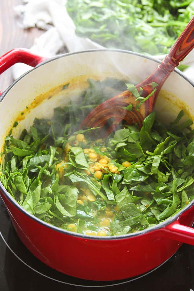 Fresh spinach being added to a pot of simmering dal.