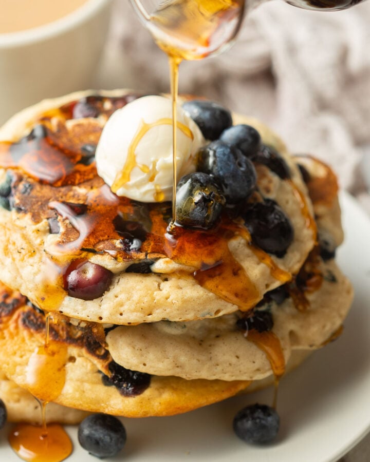 Syrup being drizzled over a stack of Vegan Blueberry Pancakes.
