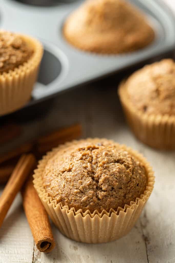 Vegan Bran Muffin with additional muffins, cinnamon sticks, and muffin tin in the background.