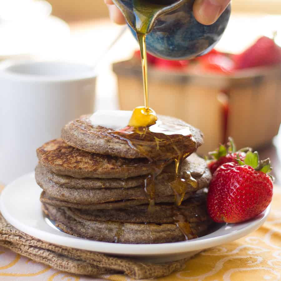 Hand pouring syrup over a stack of Vegan Buckwheat Pancakes.