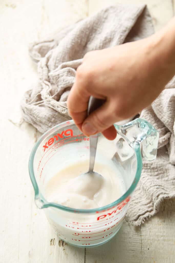 Hand stirring Vegan Buttermilk ingredients together in a liquid measuring cup.