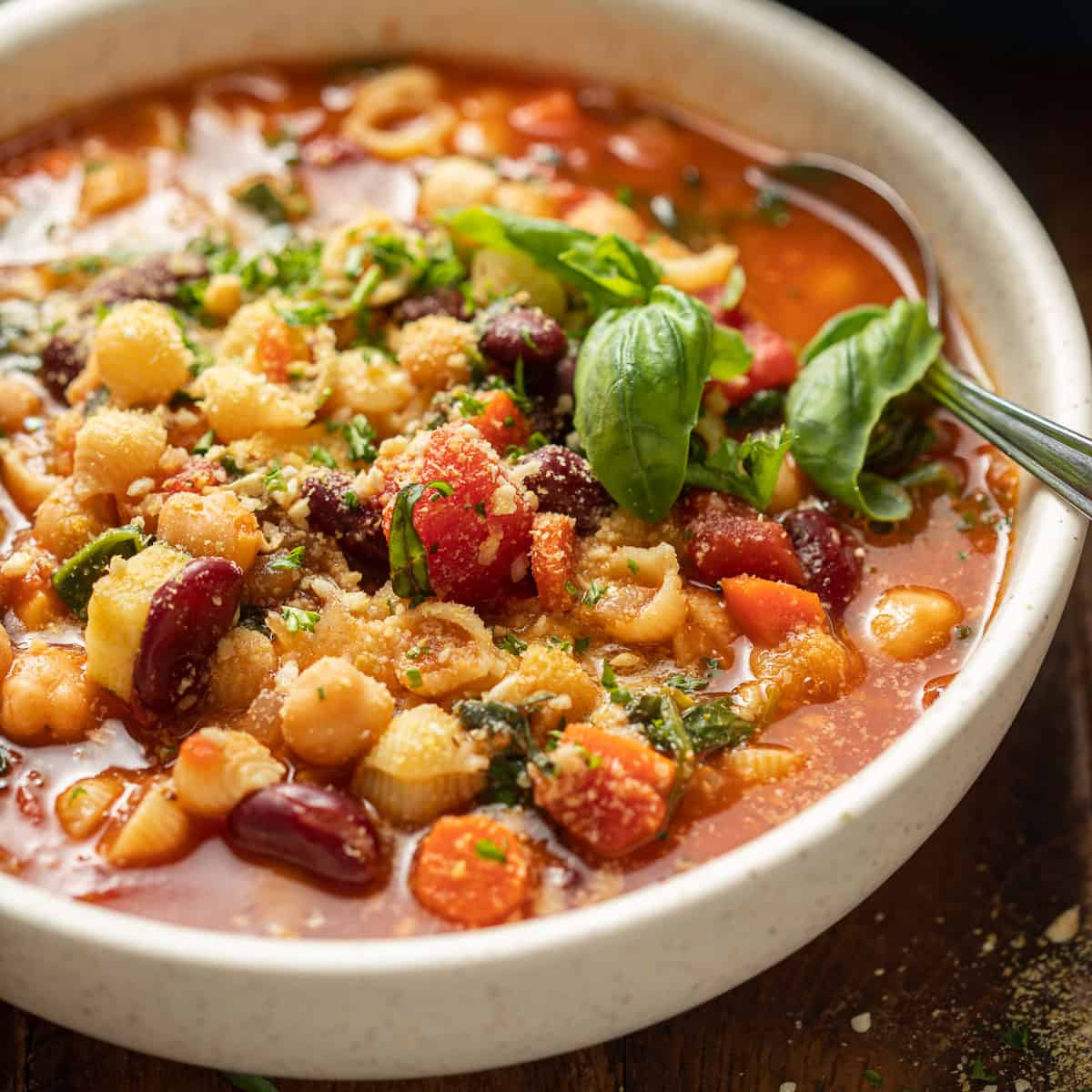 Close-up of a bowl of vegan minestrone soup topped with vegan parmesan and fresh basil.