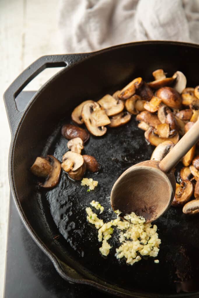 Garlic cooking in a skillet with mushrooms pushed to the side.