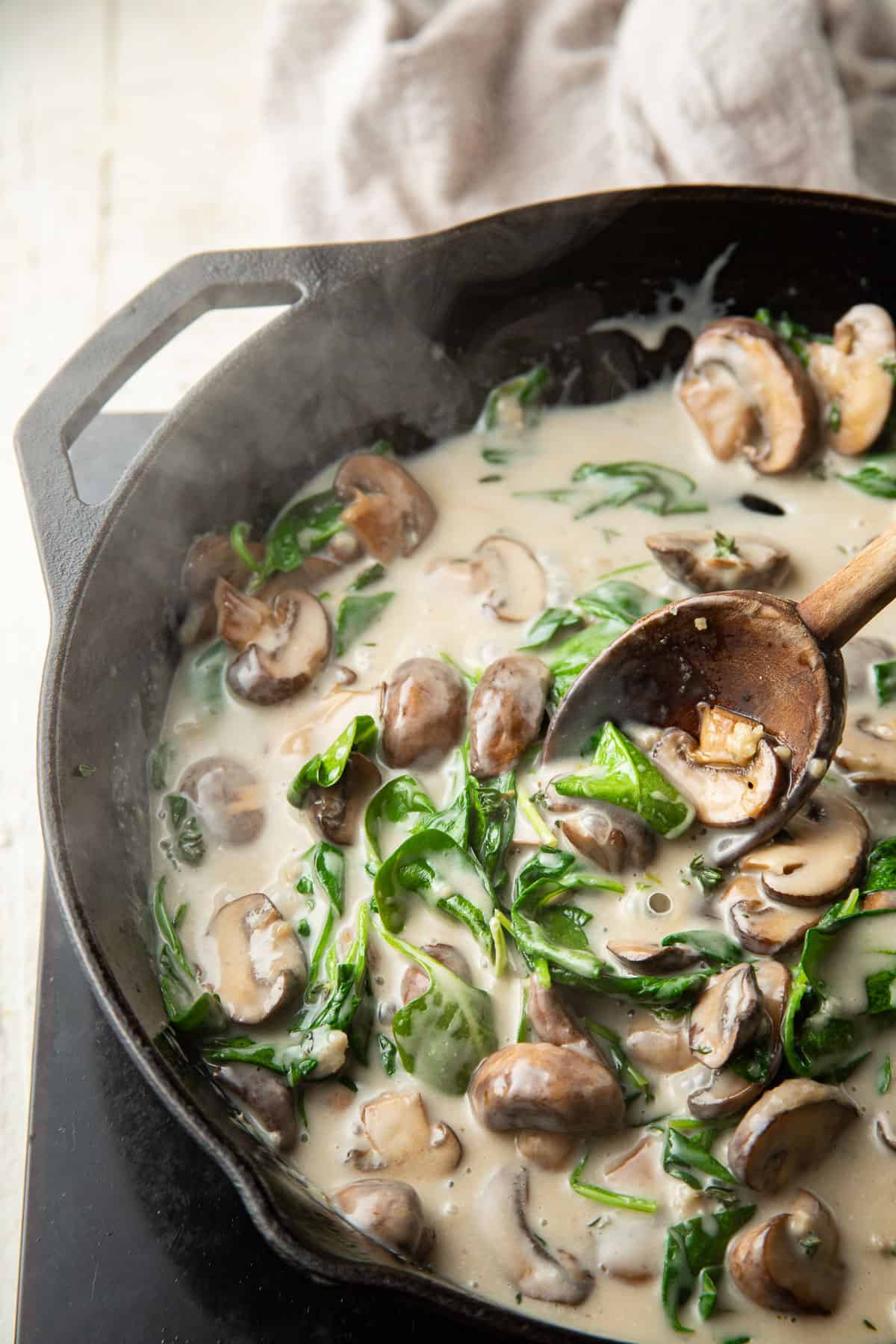 Mushrooms and spinach cooked in a creamy sauce in a skillet.