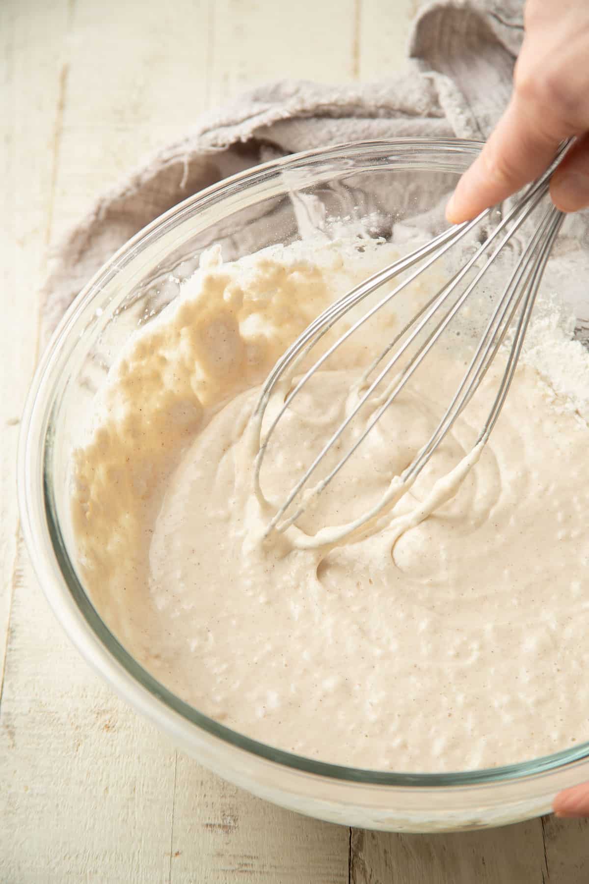 Hand whisking waffle batter in a mixing bowl.