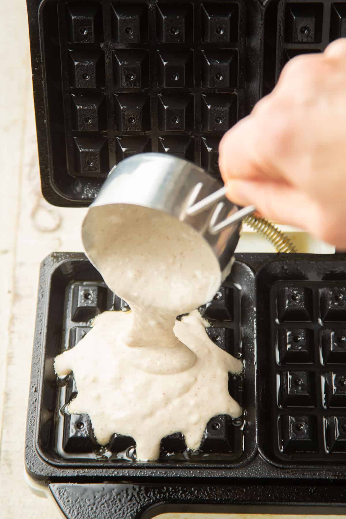 Hand pouring waffles batter into a waffle iron.
