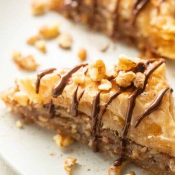 Close up of a slice of Vegan Baklava topped with chocolate and nuts on a dish.