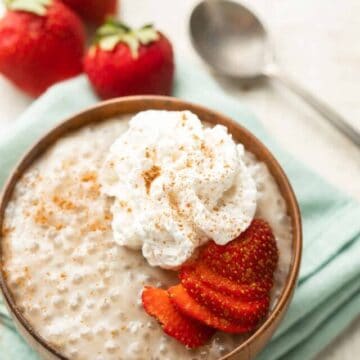 Bowl of Vegan Tapioca Pudding with spoon and strawberries in the background.