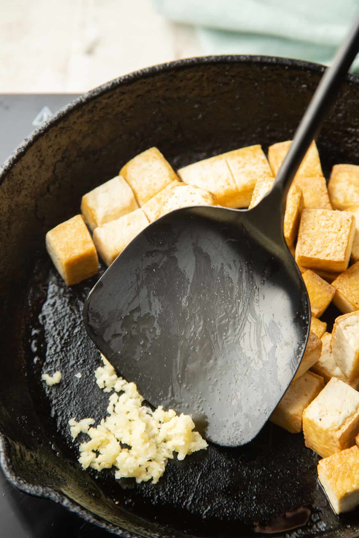 Minced garlic cooking in a skillet with tofu.