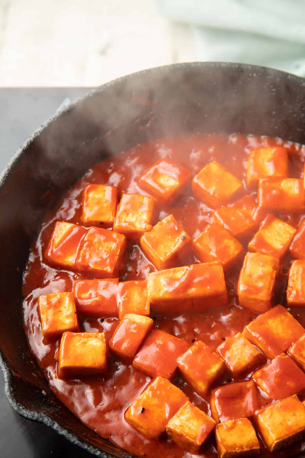 Tofu cooking in gochujang sauce in a skillet.