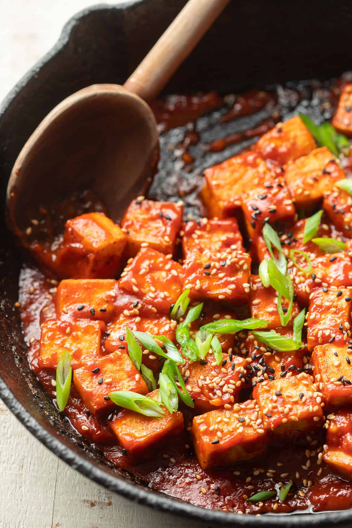 Gochujang Tofu in a skillet with a wooden spoon.