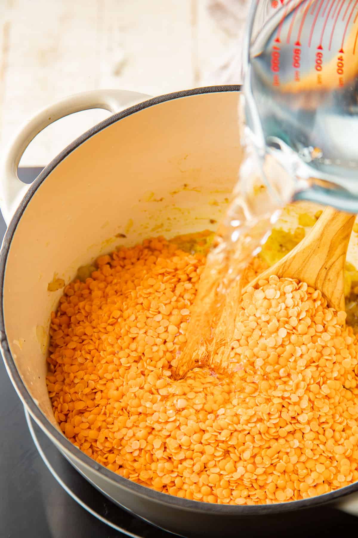 Water being poured into a pot of dry red lentils.