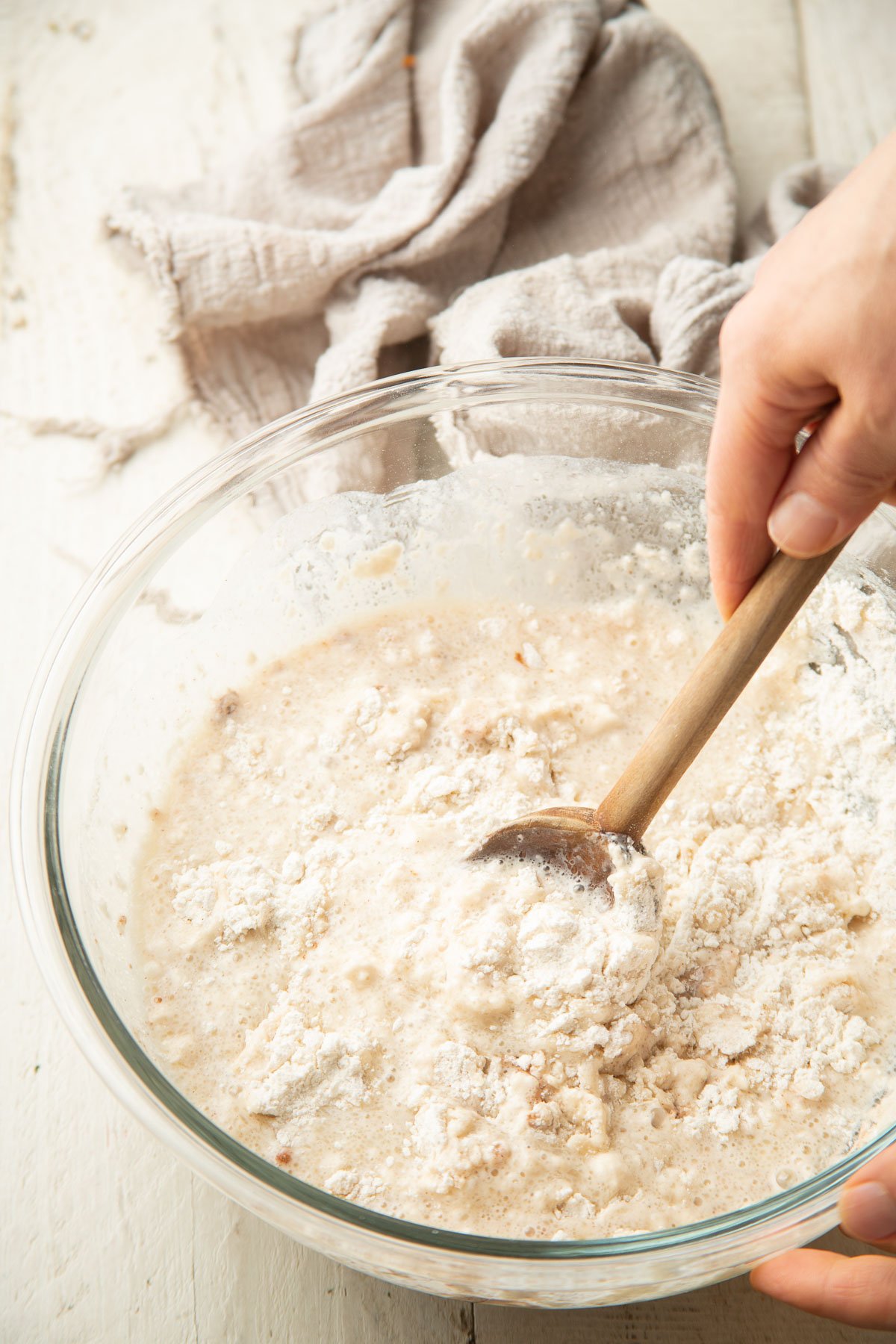 Hand stirring doughnut batter together in a glass bowl.