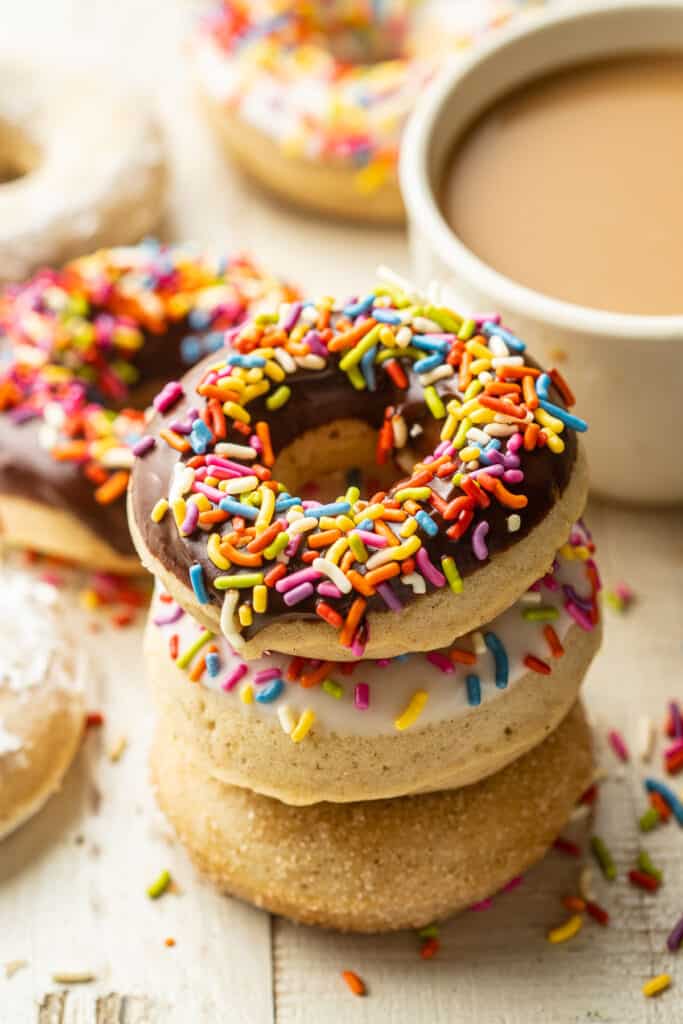 Stack of three Vegan Baked Doughnuts with a coffee cup in the background.