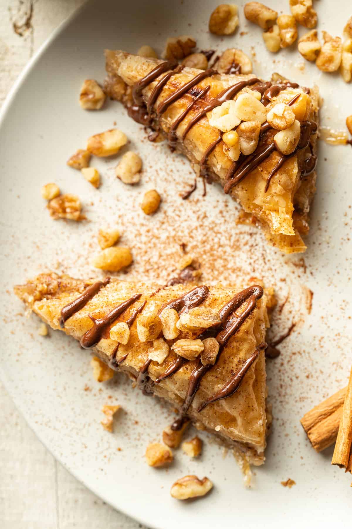 Two slices of Vegan Baklava on a dish with nuts and cinnamon sticks.