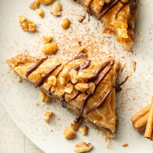 Close up of a slice of Vegan Baklava topped with chocolate and nuts on a dish.