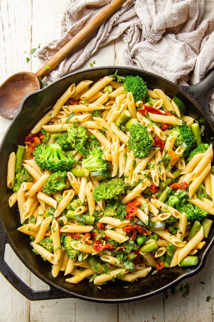 Skillet of Vegan Pasta Primavera with a wooden spoon on the side.