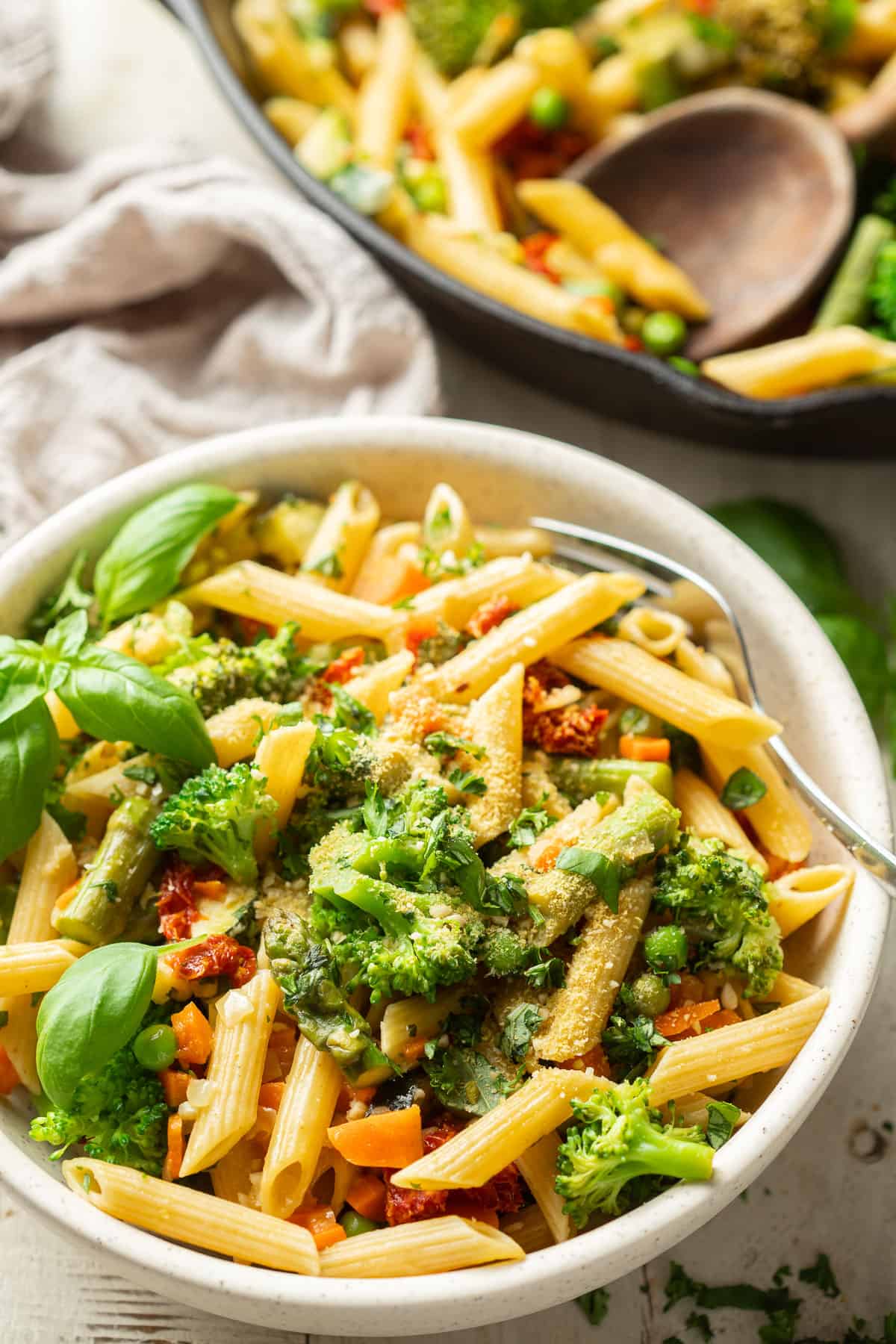 Bowl of Vegan Pasta Primavera with skillet and wooden spoon in the background.