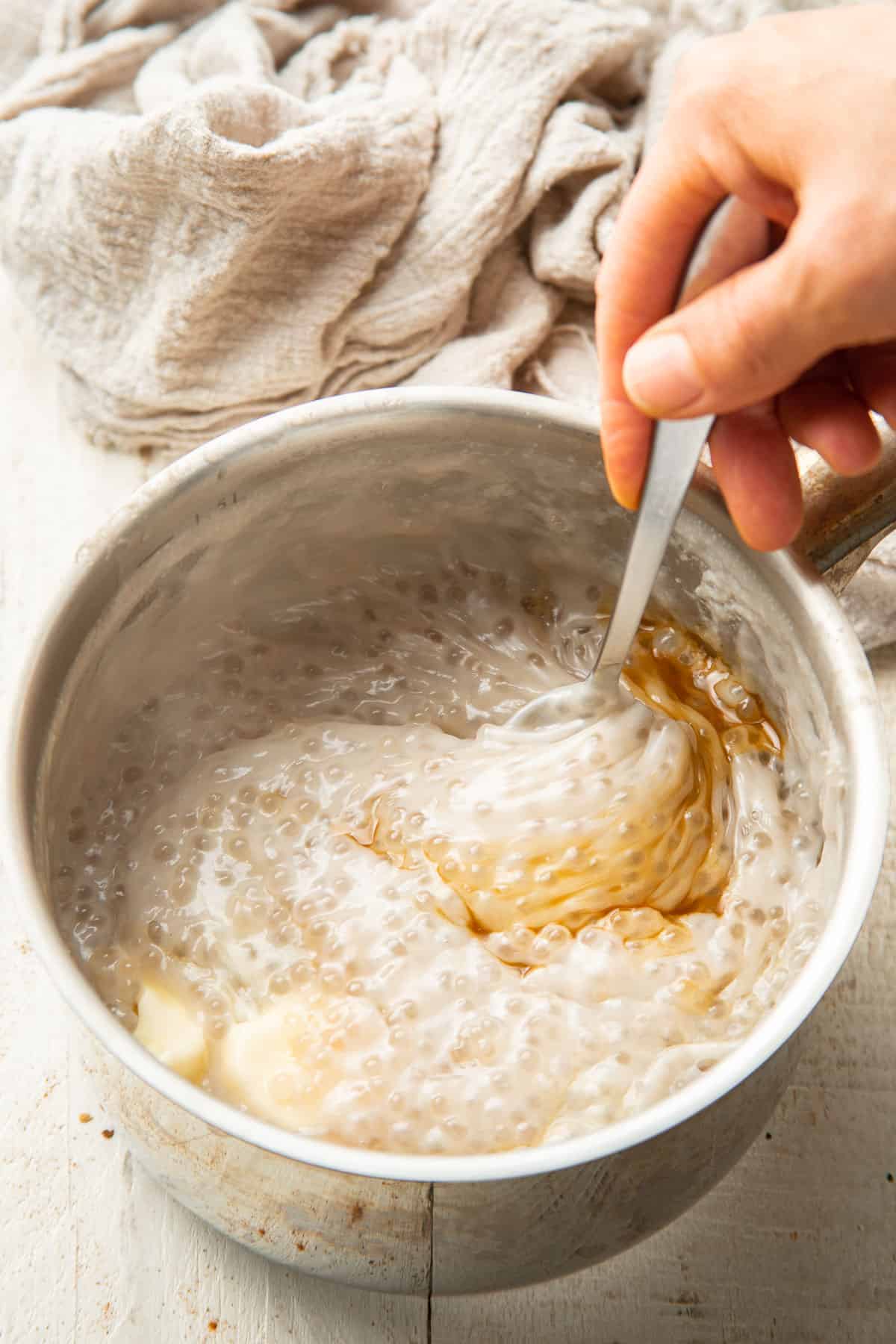 Hand stirring vanilla and vegan butter into a pot of Vegan Tapioca Pudding.