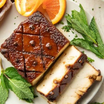 White wooden surface set with oranges, mint leaves and partially sliced tofu roast.