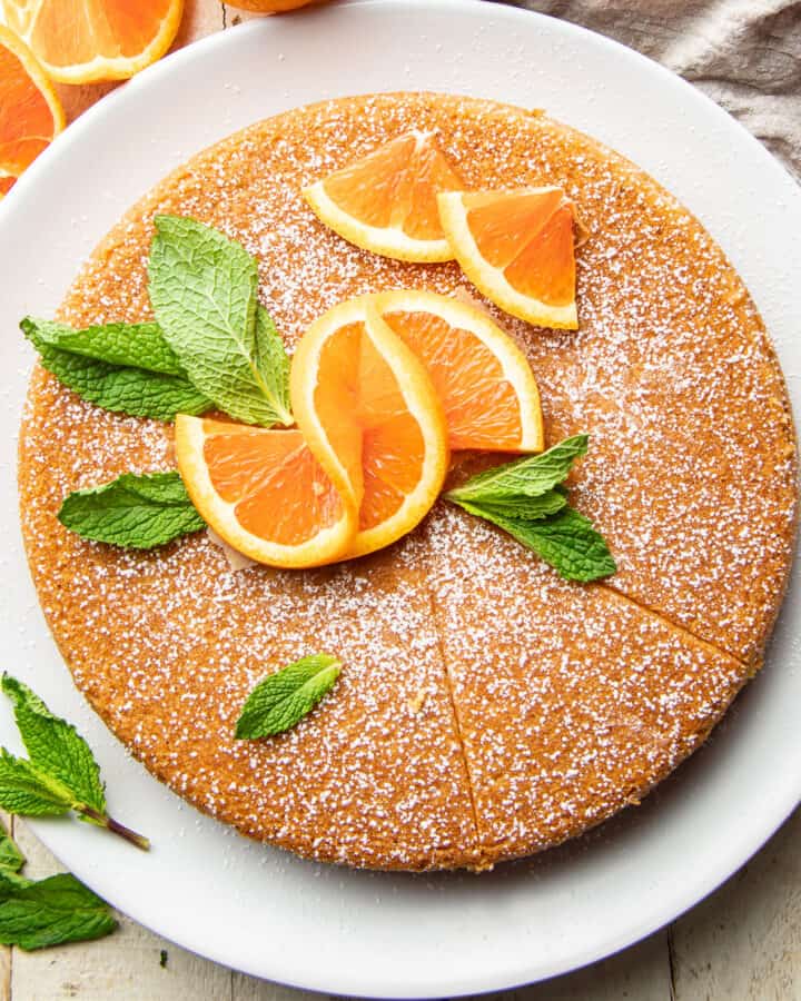Vegan Orange Olive Oil Cake on a Plate with mint leaves and orange slices on top.