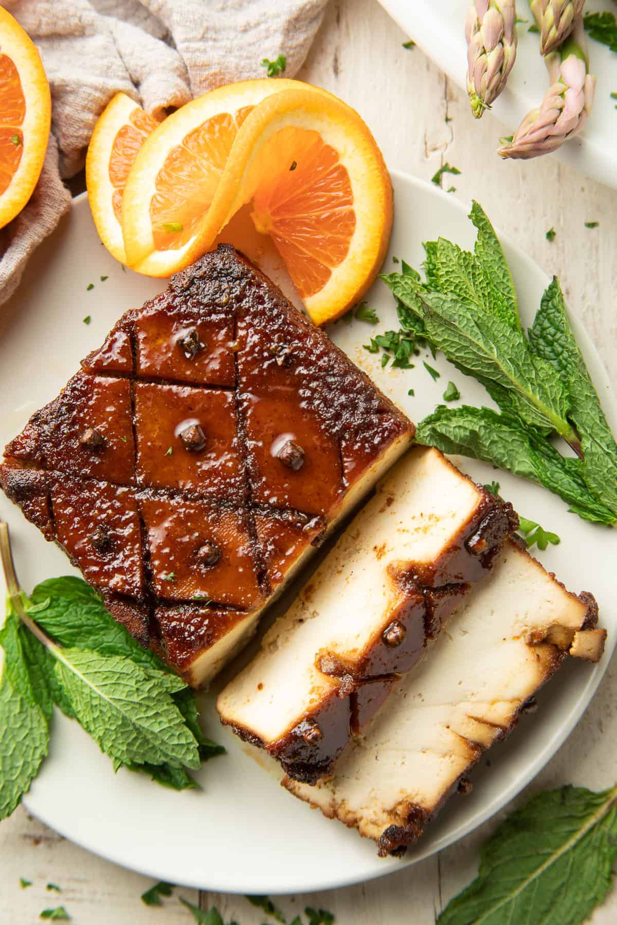 White wooden surface set with oranges, mint leaves and partially sliced tofu roast.