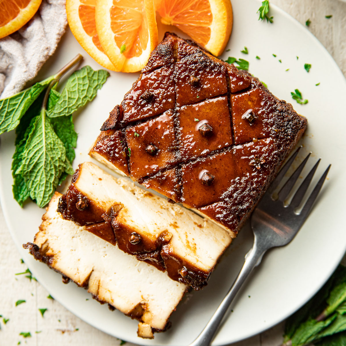 Close up of a tofu roast on a plate with mint leaves and orange slices.