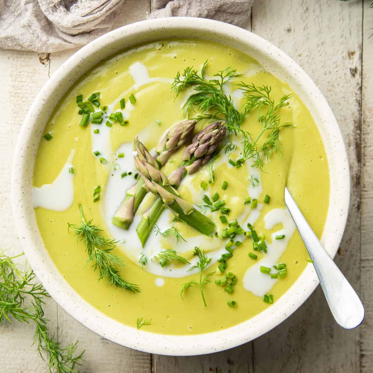 Bowl of Vegan Cream of Asparagus Soup topped with dill, chives, and asparagus tips.