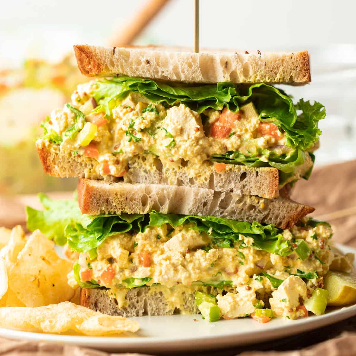 Two halves of a vegan egg salad sandwich are stacked on a plate.