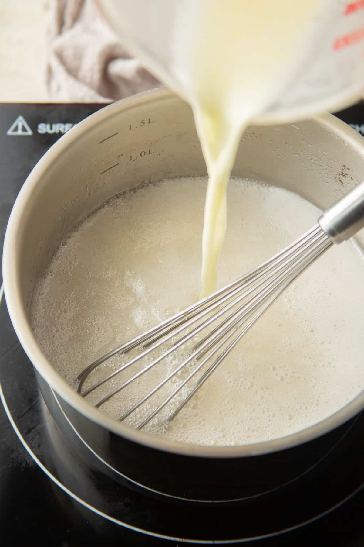 Lemon and cornstarch being poured into a saucepan of simmering coconut cream and sugar.