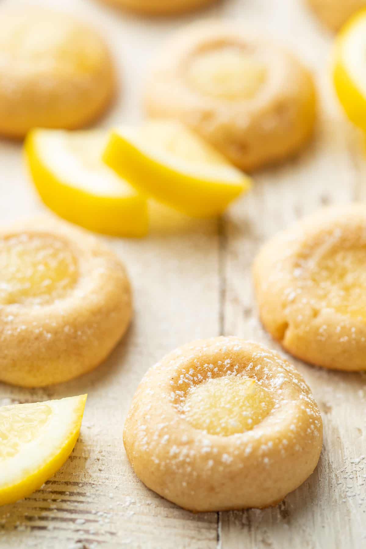 Vegan Lemon Curd Cookies on a white wooden surface with lemon slices in the background.