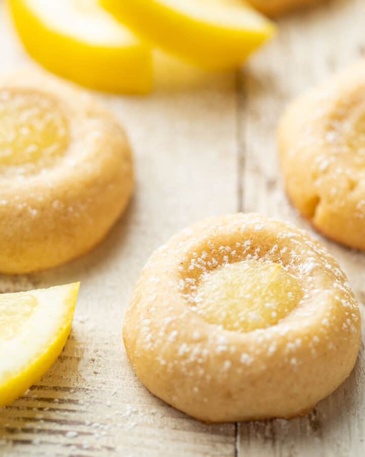 Vegan Lemon Curd Cookies on a white wooden surface with lemon slices in the background.