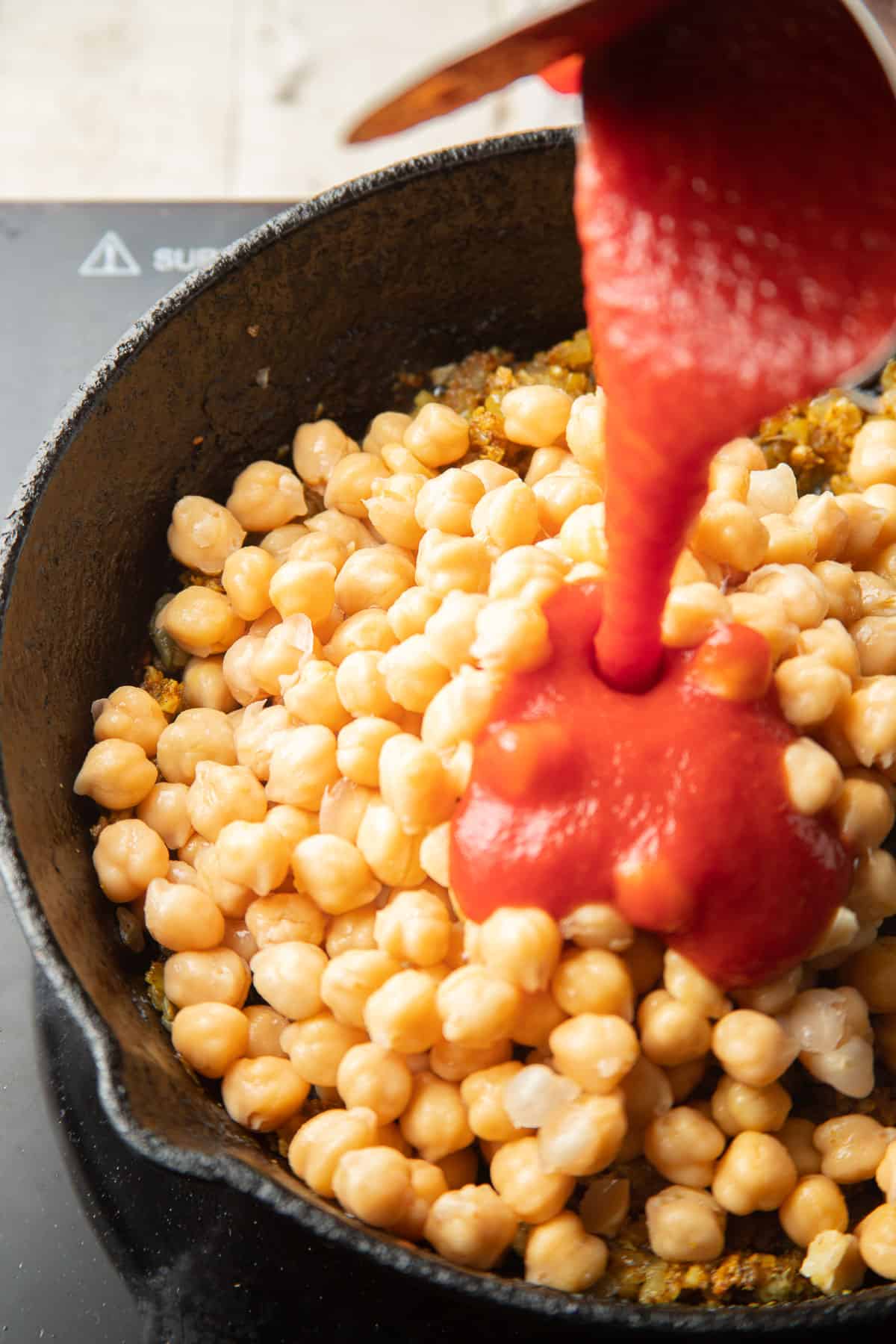 Tomato sauce being poured into a skillet of chickpeas.