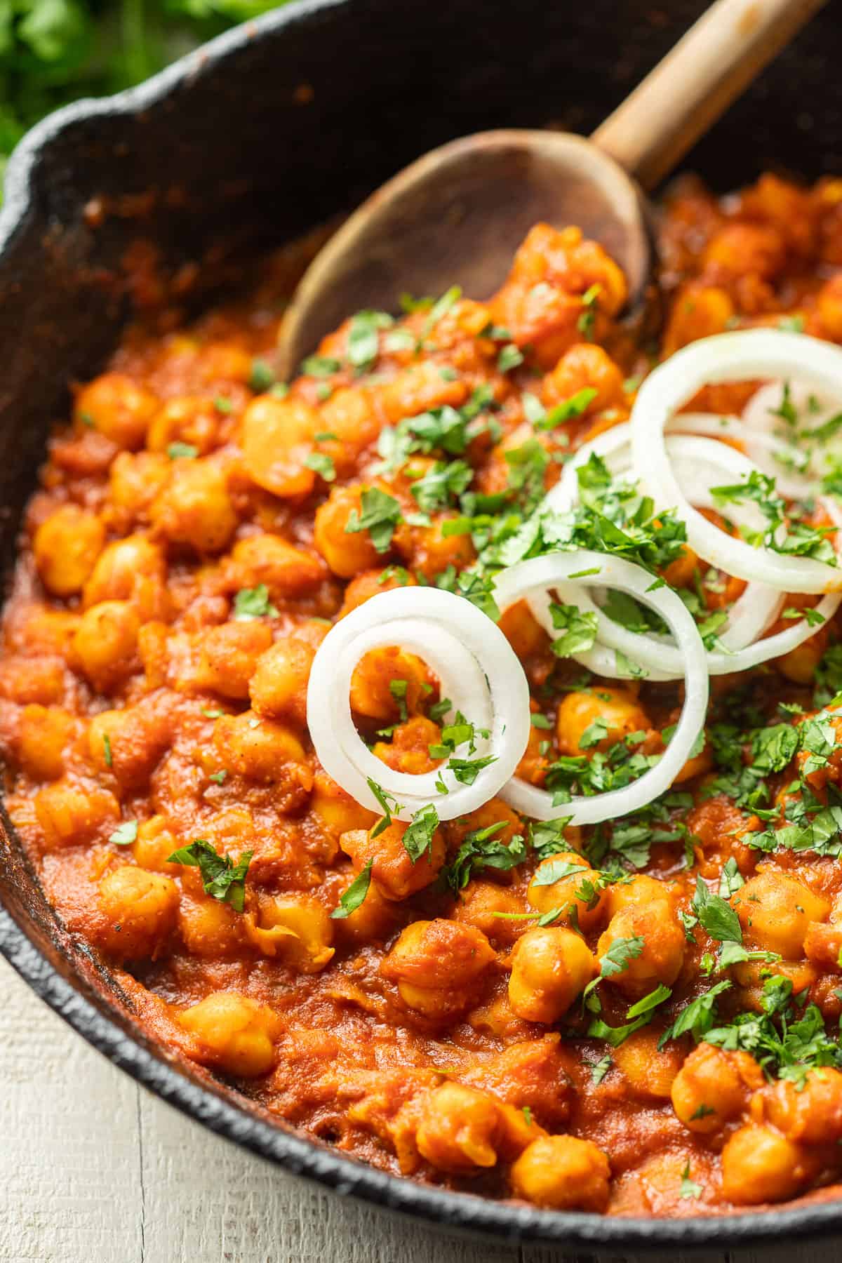 Close up of Vegan Chana Masala in a skillet with wooden spoon.