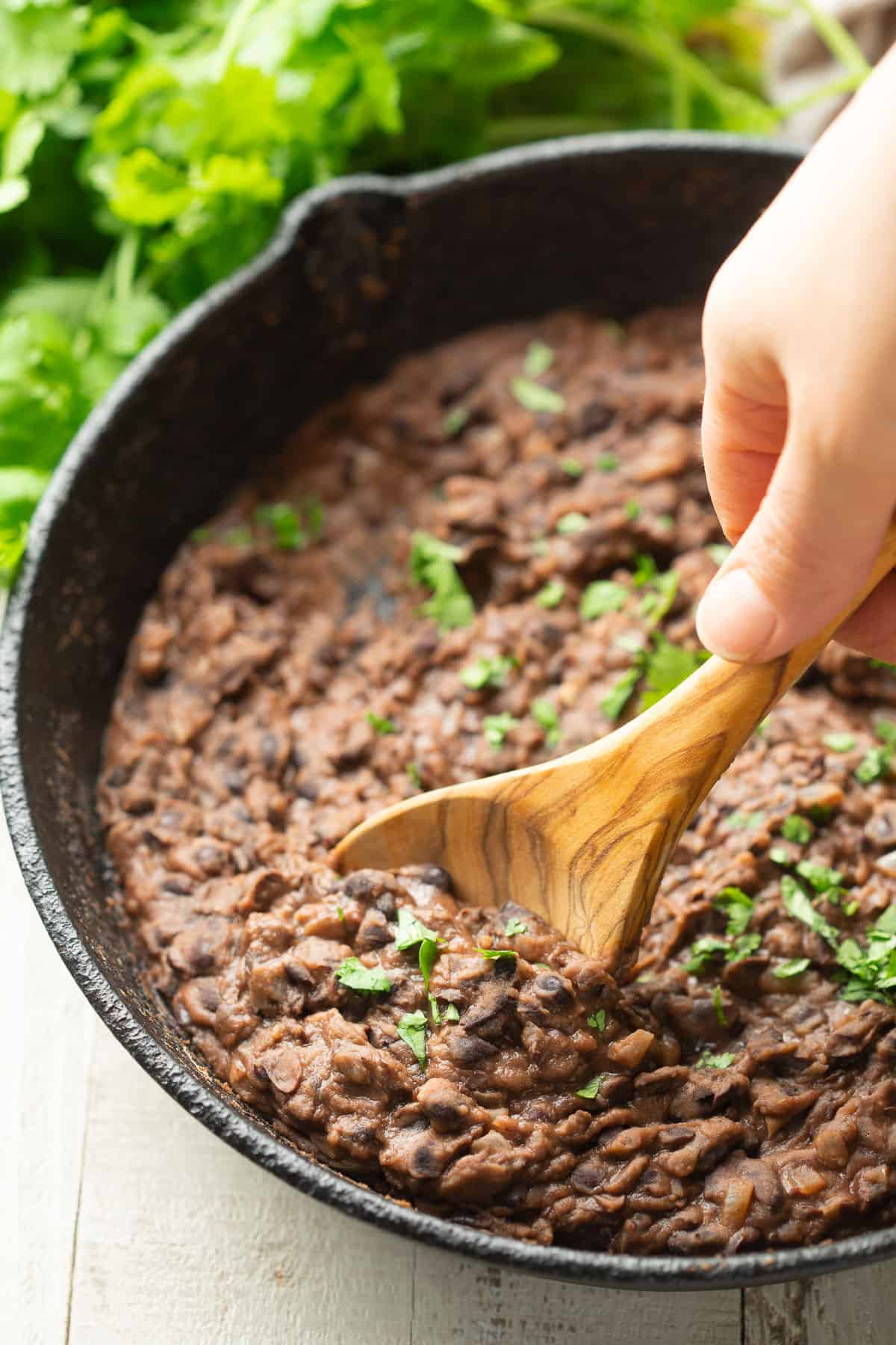 Hand with spoon scooping refried black beans from a skillet.