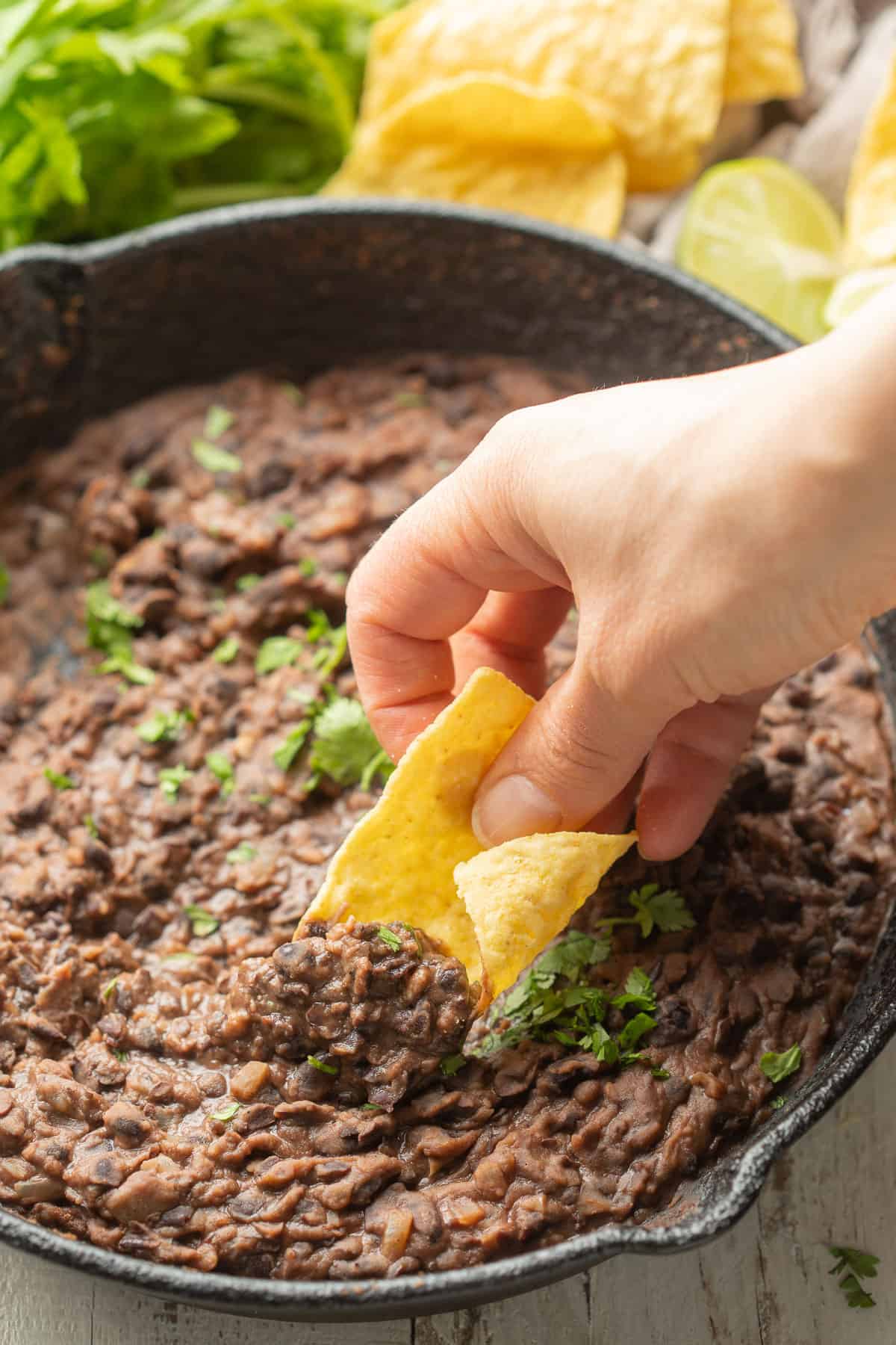 Dipping a tortilla chip hand into a skillet of refried black beans.