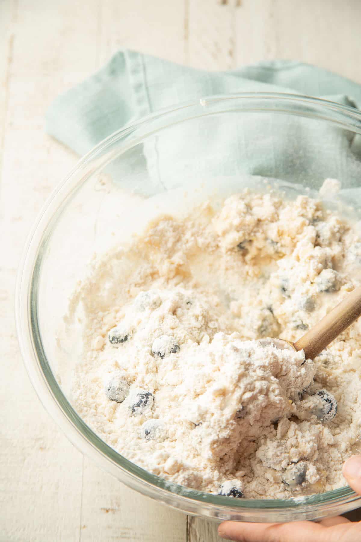 Hand stirring scone dough together in a mixing bowl.