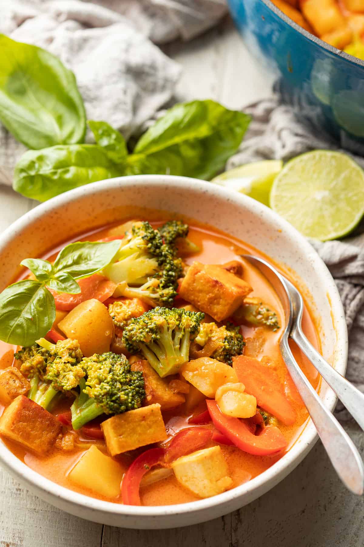 Bowl of vegan red curry with fresh basil and lime wedges in the background.