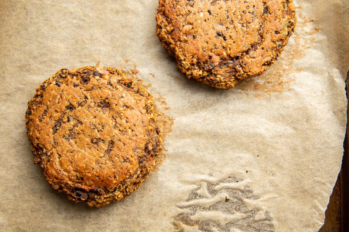 Two Sweet Potato Black Bean Burger patties on a parchment paper lined baking sheet.