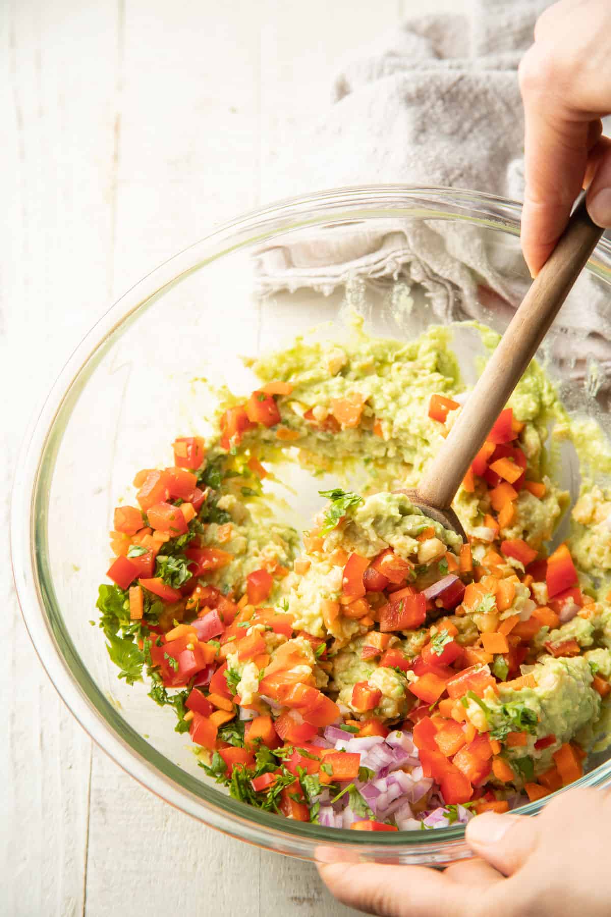 Hand stirring chickpea sandwich salad filling together in a bowl.
