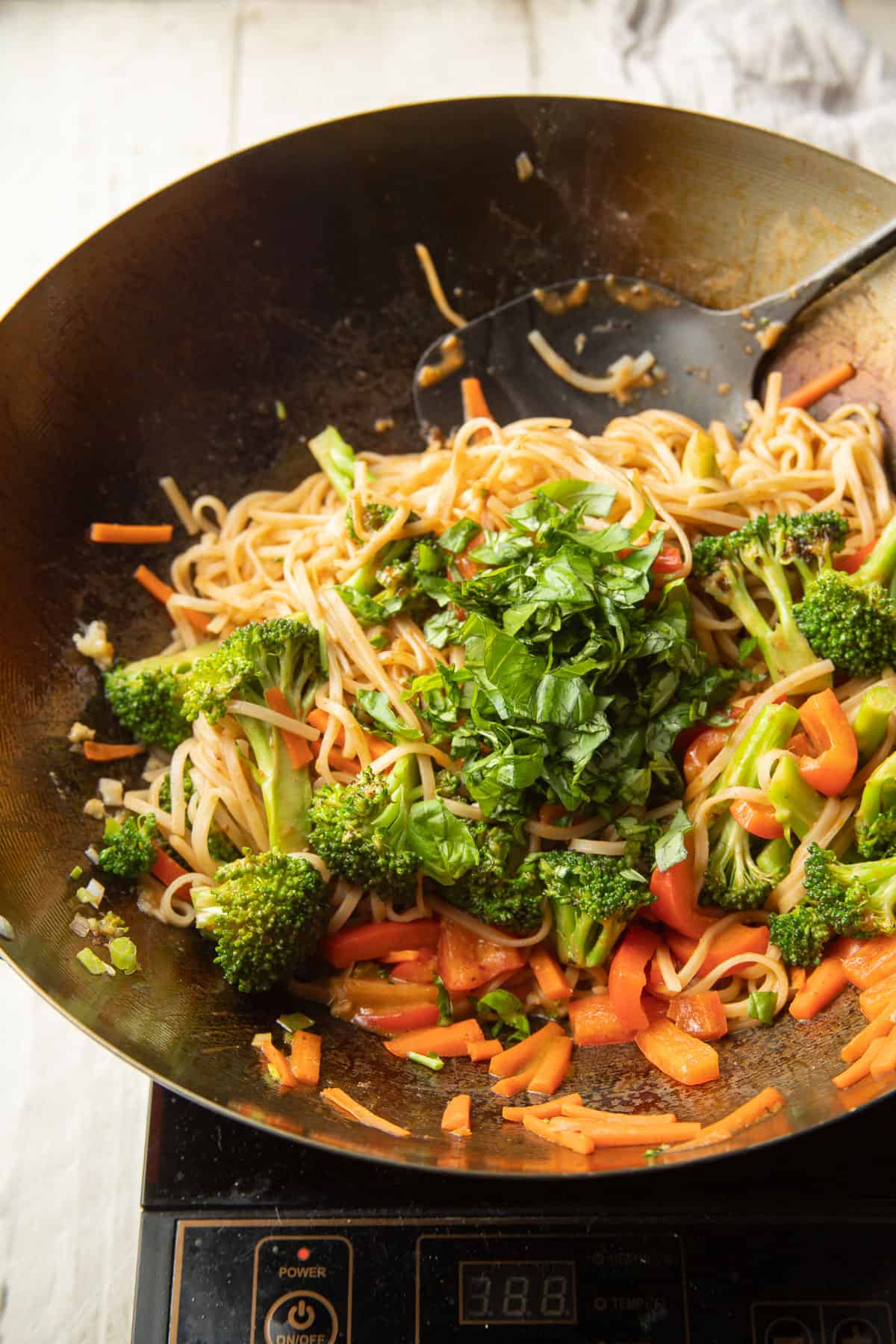 Hoisin Noodles and vegetables cooking in a wok with fresh basil on top.