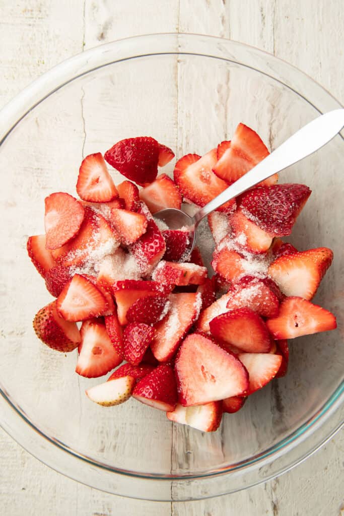 Sliced strawberries and sugar in a bowl with spoon.