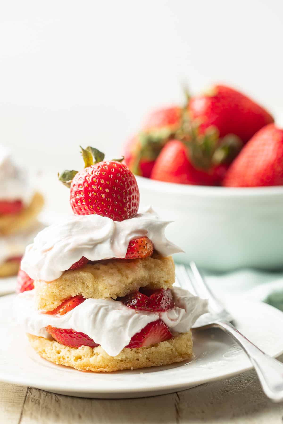 Vegan Strawberry Shortcake on a plate with a bowl of strawberries in the background.