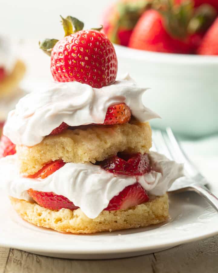 Vegan Strawberry Shortcake on a plate with bowl of strawberries in the background.